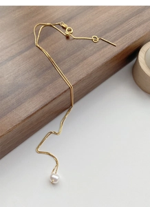 Detail of adjustable gold box chain with a white freshwater pearl on dark wood