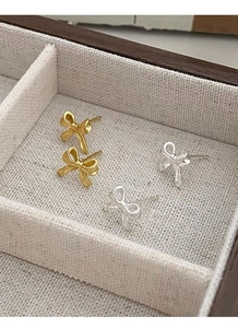 Vue macro de boucles d'oreilles nœuds dorées et argentées dans un écrin à bijoux en bois