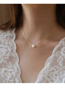 Close-up of a minimalist S925 silver necklace with a single round white pearl on a gold chain
