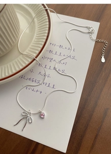 Detailed macro view of S925 silver bow and pink heart pendant on a snake bone chain