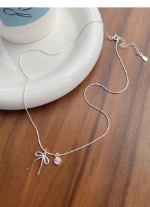 Detail of S925 silver necklace with pink heart gem and bow pendant on ceramic dish