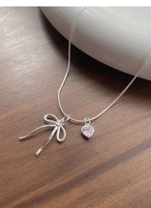 Detail of silver S925 necklace with hollow bow and pink heart crystal pendant on snake chain