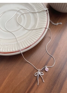 Close-up of S925 silver bow necklace with pink heart pendant on a ceramic dish