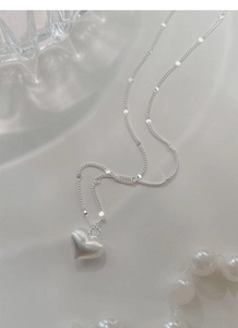 Close-up of S925 sterling silver heart necklace with brushed texture and pearl accents