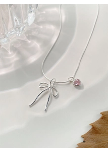 Macro detail of silver bow and pink heart pendant on a snake chain over water ripple background