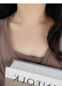 Close-up of S925 silver bow necklace with pink heart pendant on a model neck