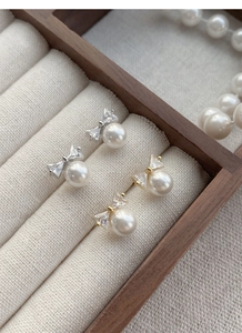 Detail view of silver and gold bow earrings with pearls in a wooden jewelry display case