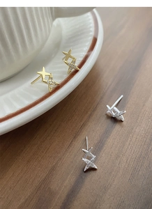 Detailed view of silver and gold star earrings with cubic zirconia on a ceramic cup