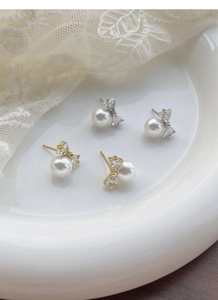 Close-up of S925 silver bow pearl earrings with zirconia stones on a ceramic tray