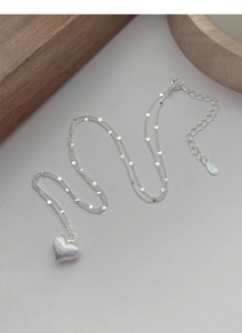 Macro detail of S925 sterling silver heart pendant with brushed finish and layered sequins