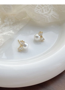 Detail of silver bow earrings with sparkling zircons and a lustrous round pearl