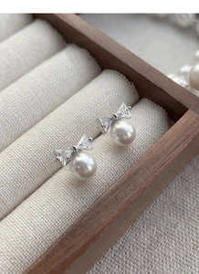 Macro shot of silver bow stud earrings with clear zircons and elegant white pearls