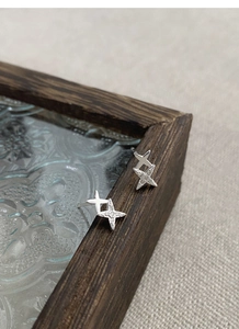 Detail view of S999 silver four-point star earrings with zircons on vintage wood