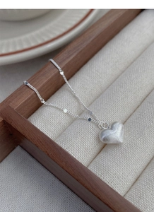 Macro detail of brushed silver heart pendant and delicate chain in a jewelry box