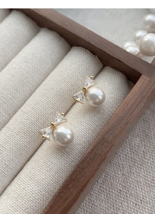 Detail of S925 silver pearl bow earrings with zircon stones on beige velvet fabric