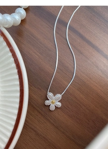 Detail of S925 silver daisy necklace with enamel petals on a dark wood background