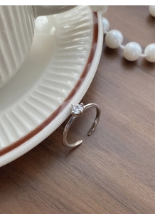 Macro shot of silver ring featuring a four-prong round zircon on a textured ceramic dish