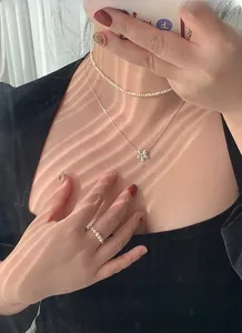 Close-up of layered S925 silver daisy necklace and pearl ring set on female model