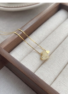 Détail du collier double cœur doré avec zircons cubiques pavés sur un coffret en bois