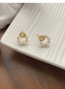Vue détaillée des boucles d'oreilles camélia doré et perles sur un plateau blanc