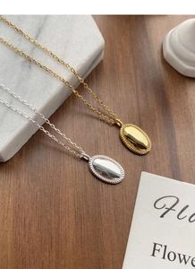 Details silberner und goldener Oval-Anhänger mit Spiegelglanz auf Marmor und Holz