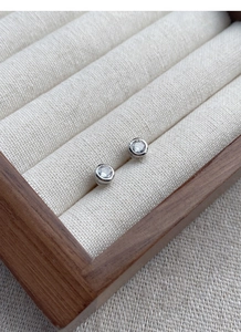 Detail of minimalist S925 silver stud earrings with small zircon on beige jewelry stand