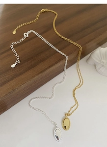 Nahaufnahme goldener und silberner Oval-Anhänger mit Perlenrand an feinen Ketten