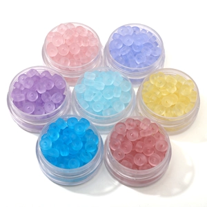 Dettaglio di sette vasetti di perline in vetro smerigliato in colori pastello per gioielli DIY