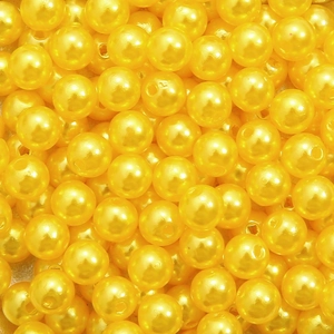 Macro shot of bright yellow round acrylic pearl beads with pre-drilled holes for DIY jewelry