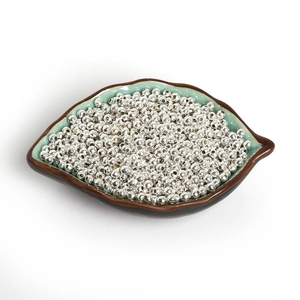 Close-up of bulk silver iron spacer beads for DIY jewelry making in a leaf ceramic tray