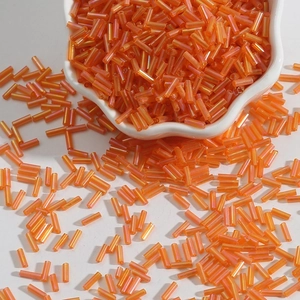 Macro shot of orange aurora glass tube beads in a white ceramic dish for DIY jewelry