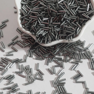 Macro detail of silver gray bugle beads spilling from a white bowl for DIY jewelry projects