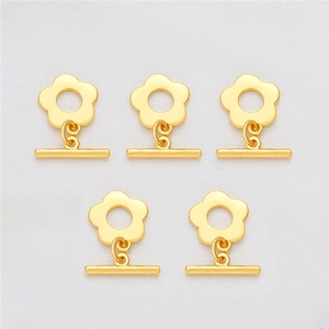 Macro detail of five 18K gold-plated floral toggle clasps on white silk background