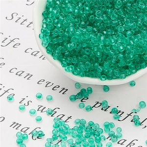 Close-up of translucent green glass seed beads in a ceramic bowl for DIY jewelry making
