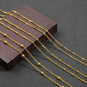Detail of assorted golden iron ball and O-link chains on dark wood for DIY accessories