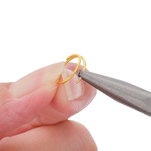Goldene Spaltringe aus Eisen für DIY-Schmuckherstellung mit Zange auf weißem Hintergrund