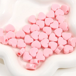 Vue macro de perles en cœur acrylique rose dans un plateau blanc pour bijoux DIY