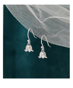 Gros plan de boucles d'oreilles muguet en argent S925 sur fond de maille vert et blanc