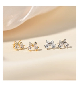 Détail de boucles d'oreilles nœuds argent et or avec zircons sur du satin
