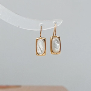 Detail view of gold S925 silver shell earrings hanging on a transparent display stand