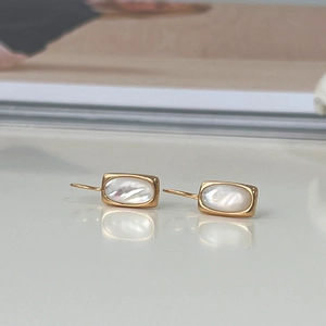 Detail of elegant gold S925 silver shell earrings on a white reflective background