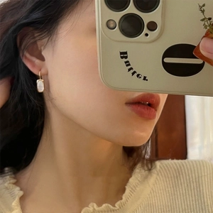 Close-up of gold oval shell earrings worn by a model in a minimalist lifestyle setting