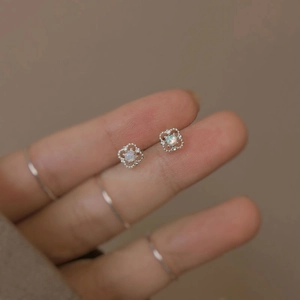 Detailed close-up of S925 silver hollow floral earrings with opal stones on fingertips
