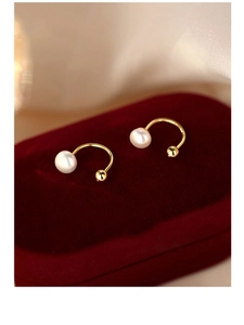 Macro shot of gold U-shaped silver earrings with glossy white freshwater pearls on red velvet