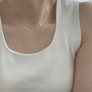Detail of a minimalist layered S925 silver necklace with a tiny cross pendant on model