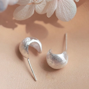 Vue détaillée de boucles d'oreilles courbées en argent brossé sur cuir beige doux