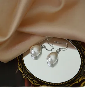 Detailed view of teardrop pearl earrings on a vintage gold mirror with champagne silk
