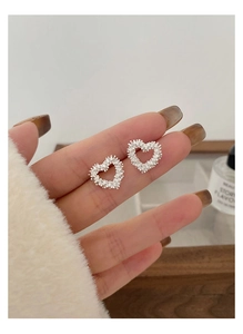 Close-up of heart-shaped silver earrings with sparkling textured surface held by hand