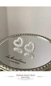 Macro detail of S925 sterling silver hollow heart stud earrings on a vintage mirror surface