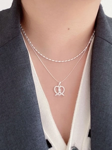 Detail of twisted silver necklace featuring a knotted heart pendant on a model